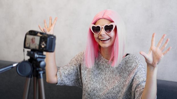 Happy girl blogger in pink wig in front of the camera on a tripod. She records a video blog