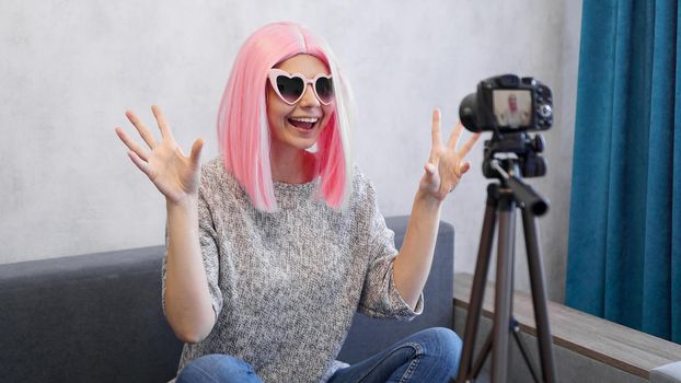 Happy girl blogger in pink wig in front of the camera on a tripod. She records a video blog