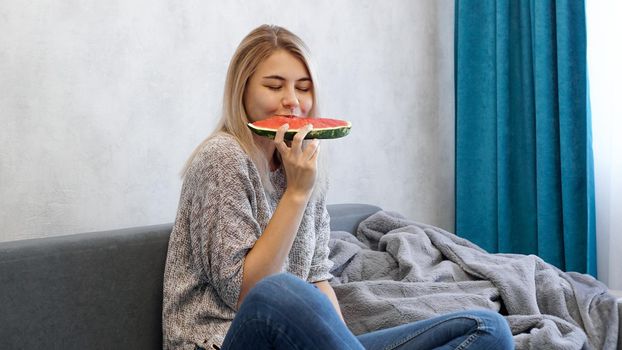 Young attractive woman bites a piece of watermelon. Woman at home in a cozy interior