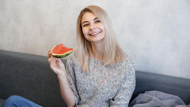 Young attractive woman eating watermelon. Woman at home in a cozy interior looking at camera and smiling