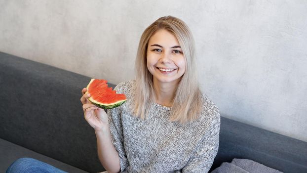 Young attractive woman eating watermelon. Woman at home in a cozy interior looking at camera and smiling