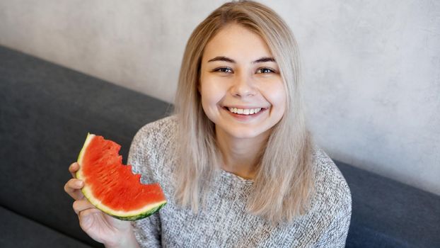 Young attractive woman eating watermelon. Woman at home in a cozy interior looking at camera and smiling