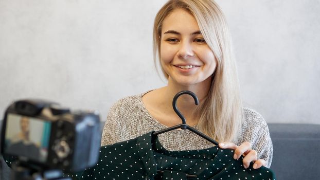 Fashion blogger recording video for blog. Woman in front of the camera holding a green dress in her hands. Close up portrait