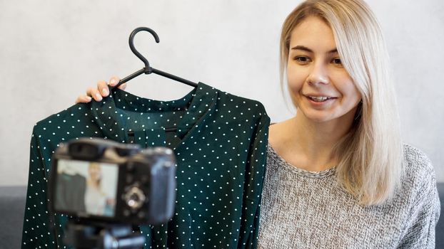 Fashion blogger recording video for blog. Woman in front of the camera holding a green dress in her hands. Close up portrait