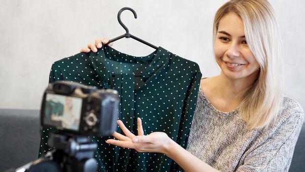 Fashion blogger recording video for blog. Woman in front of the camera holding a green dress in her hands. Close up portrait