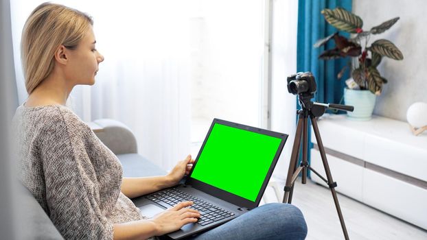 Woman blogger working on laptop. View of camera on tripod and laptop with green screen chromakey