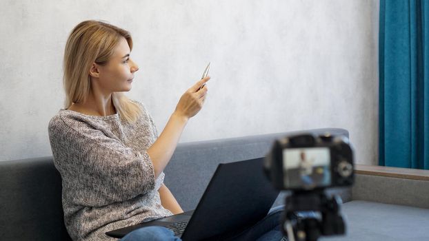 Young female blogger with laptop and pen. She talks about business or records a lecture. Woman shows with a pen on a gray wall. Place for information