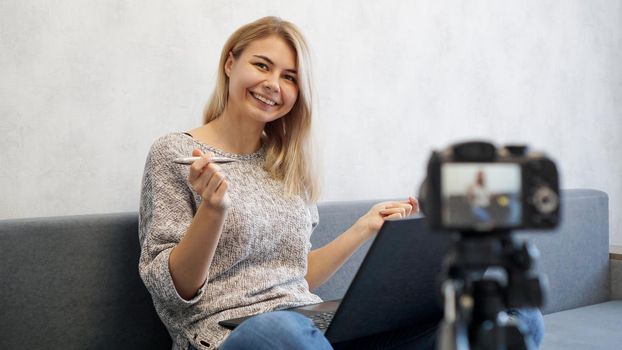 Young female blogger with laptop and pen. She talks about business or records a lecture for students. She is positive and smiling.