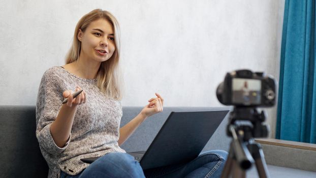 Young female blogger with laptop and pen looking at camera. She talks about business or records a lecture for students