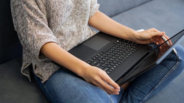 Woman using laptop with blank screen while sitting on sofa in home interior back view