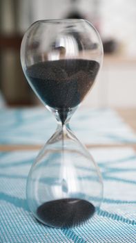 Closeup of hourglass on a white wooden table with defocus kitchen on background. Concept of time to cook.