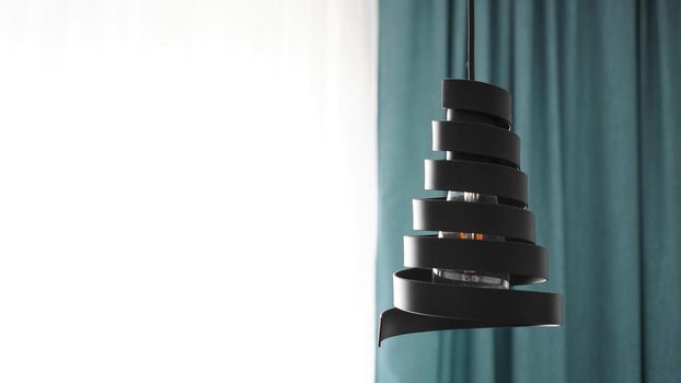 A modern loft chandelier made of black metal spiral in a stylish white and green interior