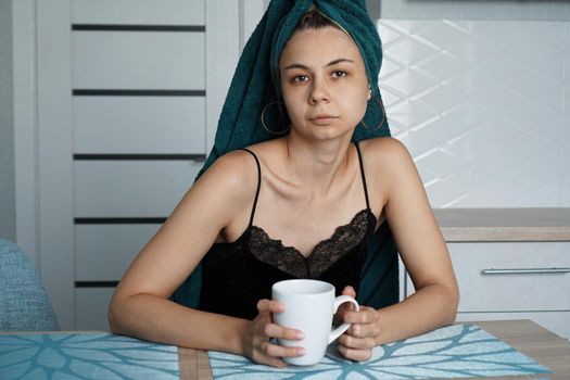 Beautiful woman in a towel on hair with a cup of coffee. Woman looking at camera