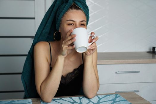 Beautiful woman sits in the kitchen with a cup of coffee. Woman drinks tea or coffee