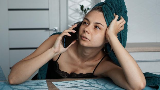 Young woman in kitchen. Talking on phone after bathing. Woman in towel