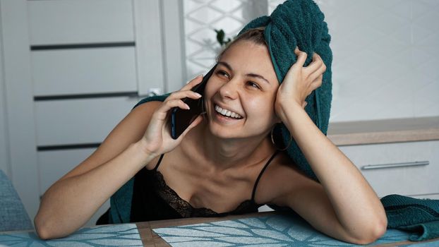 Young woman in kitchen. Talking on phone and smile. Breakfast after bathing. Woman in towel