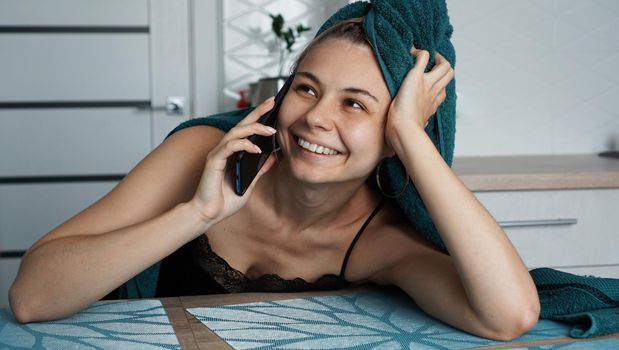 Young woman in kitchen. Talking on phone and smile. Breakfast after bathing. Woman in towel