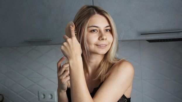 Young beautiful woman straightening her blonde hair at home - blurred grey background