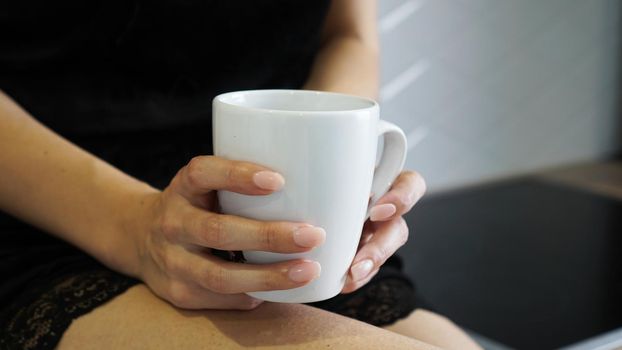 A closeup shot of the female holding a white cup in her hand at kitchen
