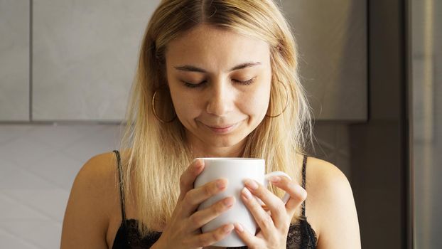 Close up of a woman taking in smell of coffee with her eyes closed in the kitchen