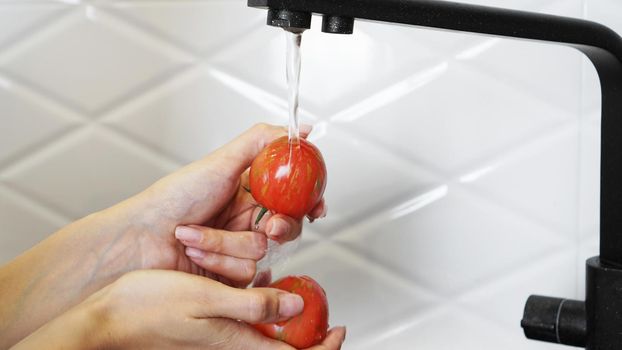 Woman washing tomatoes and tomato in her hands - white kitchen background