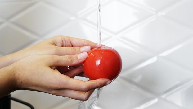 Woman washing tomatoes and tomato in her hands - white kitchen background