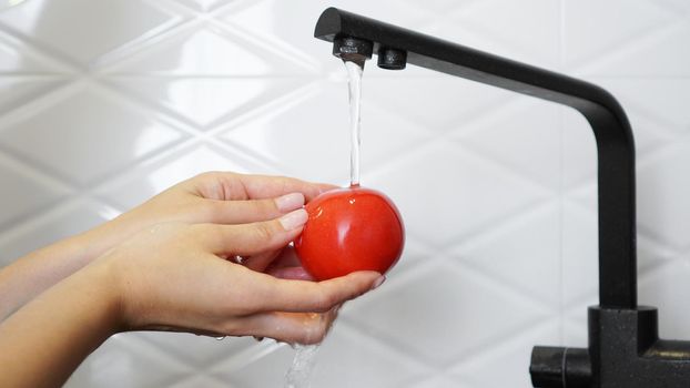 Woman washing tomatoes and tomato in her hands - white kitchen background