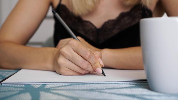 Woman hand use pencil writing on clear white sheet. White cup. Remote work or study