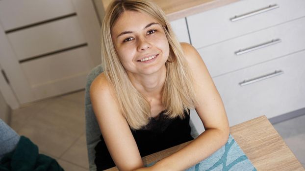 Cheerful young female sitting at table in cozy styled room while smiling and looking at camera