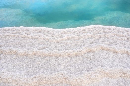 Shore of Dead sea in Ein Bokek, Israel, white salt crystals outside and at the bottom, turquoise clear water.