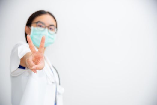 Studio portrait beautiful Asian young woman doctor raise two V shape finger wear a mask to safety Coronavirus to support in the fight against disease epidemic COVID 19 concept on blank gray background