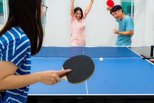 Couple fun playing table tennis or Ping pong indoor together leisure with competing in sports games at house. Father mother and daughter Asian family enjoy recreation exercise stay at home in Thailand