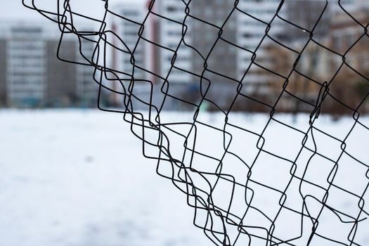 Torn mesh fence on the background of high houses close up