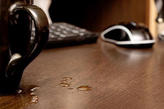 Spilled drink from the cup on the background of the computer