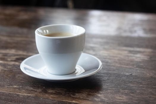 White cup of coffee on a wooden table close up