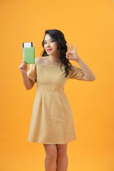 Beautiful portrait young asian woman smiling gesture ok over yellow background, holding passport.