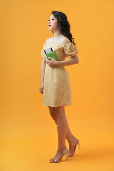 Portrait of a young female traveler with an international passport in hand over a yellow background