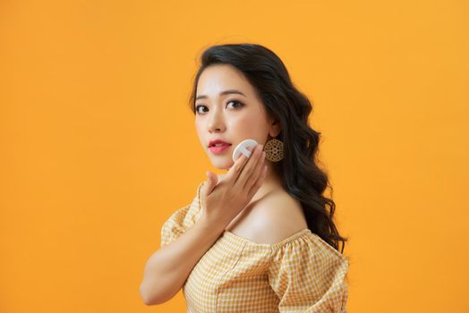 Attractive Asian woman applying foundation powder puff on her face to cover flaws and change the natural skintone. 