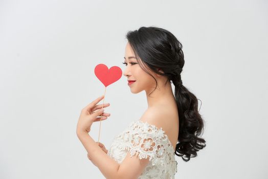 Elegant asian woman in white dress holding red heart on stick with smile