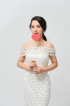 Elegant asian woman in white dress holding red heart on stick with smile