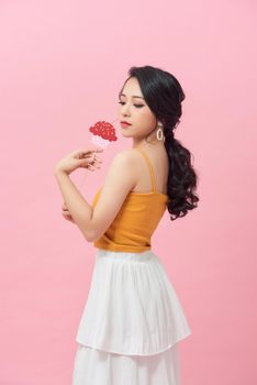 Pink background happy woman holding cakes make from paper on a stick