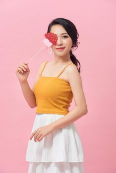 Happy young woman holding paper cupcake on stick over pink background