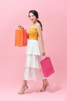 Full length portrait of a beautiful young woman posing with shopping bags, isolated against pink background