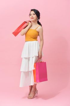 Full length portrait of a beautiful young woman posing with shopping bags, isolated against pink background