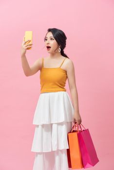 Surprised young woman with mobile phone and shopping bags on color background