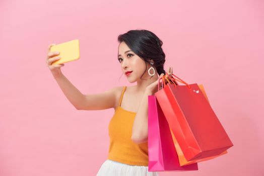 Portrait smiling woman holding packages bags with purchases after shopping doing selfie shot on mobile phone