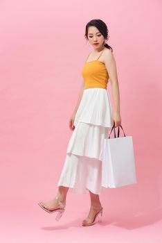 Full length side view of young woman walking with shopping bag isolated over pink background