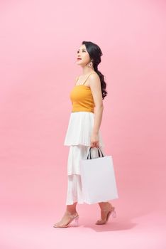 Charming young Asian woman happily shopping during sale season isolated on pink background.