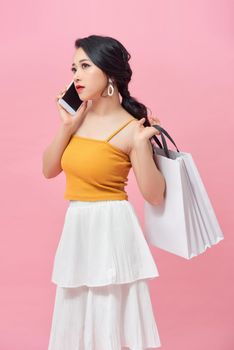 Attractive woman using a mobile phone and carrying some shopping bags over pink background.