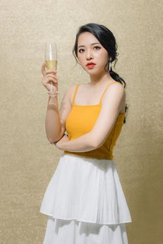 Attractive young Asian woman holding wine glass isolated over gold background. 